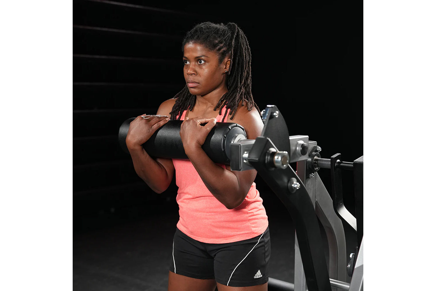 Woman wearing neon pink sleeveless tank top and black shorts performing dumbbell exercise on weight machine