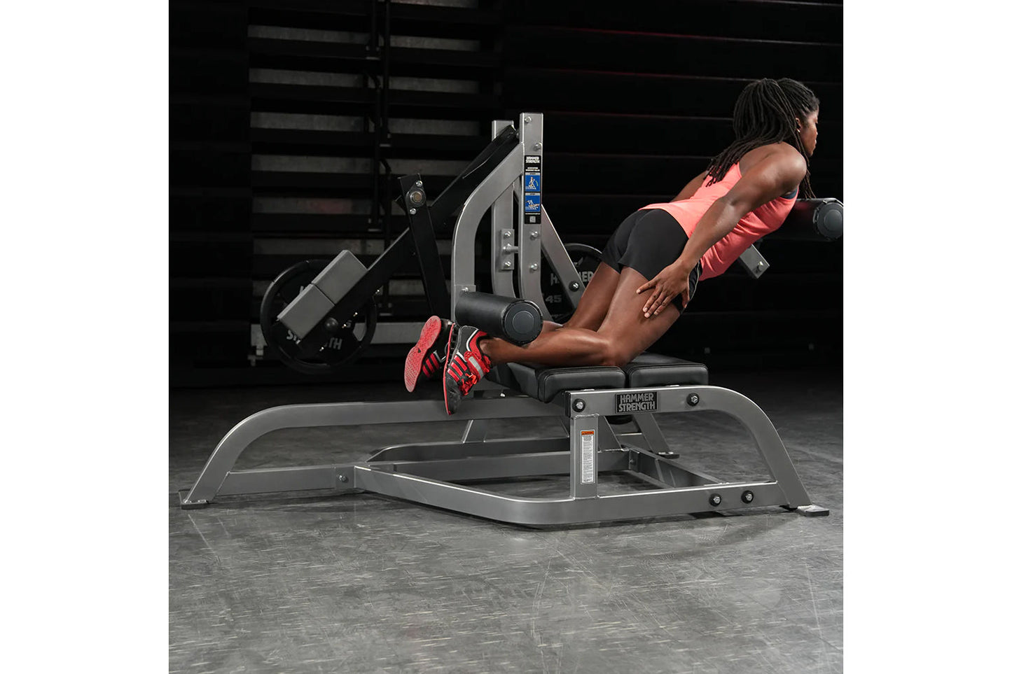 Woman using black and gray Hammer Strength leg press machine with red sneakers in gym setting