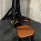 Black and tan leather leg press machine with brown padded seat and foot plates, displayed on gray rubber flooring against con