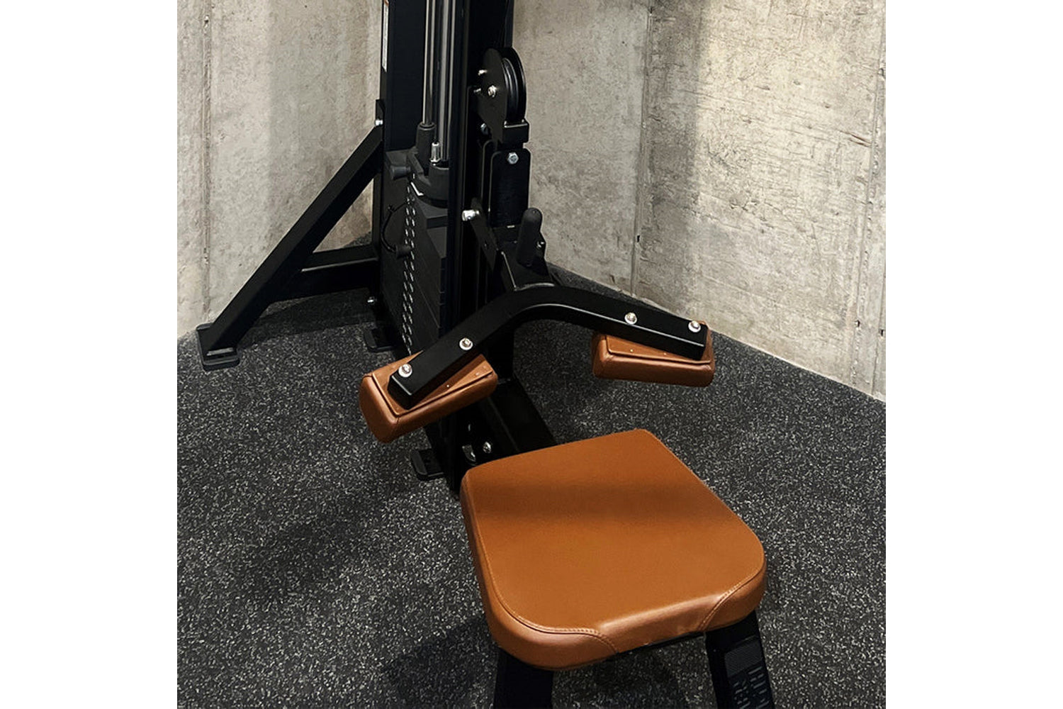Black and tan leather leg press machine with brown padded seat and foot plates, displayed on gray rubber flooring against con