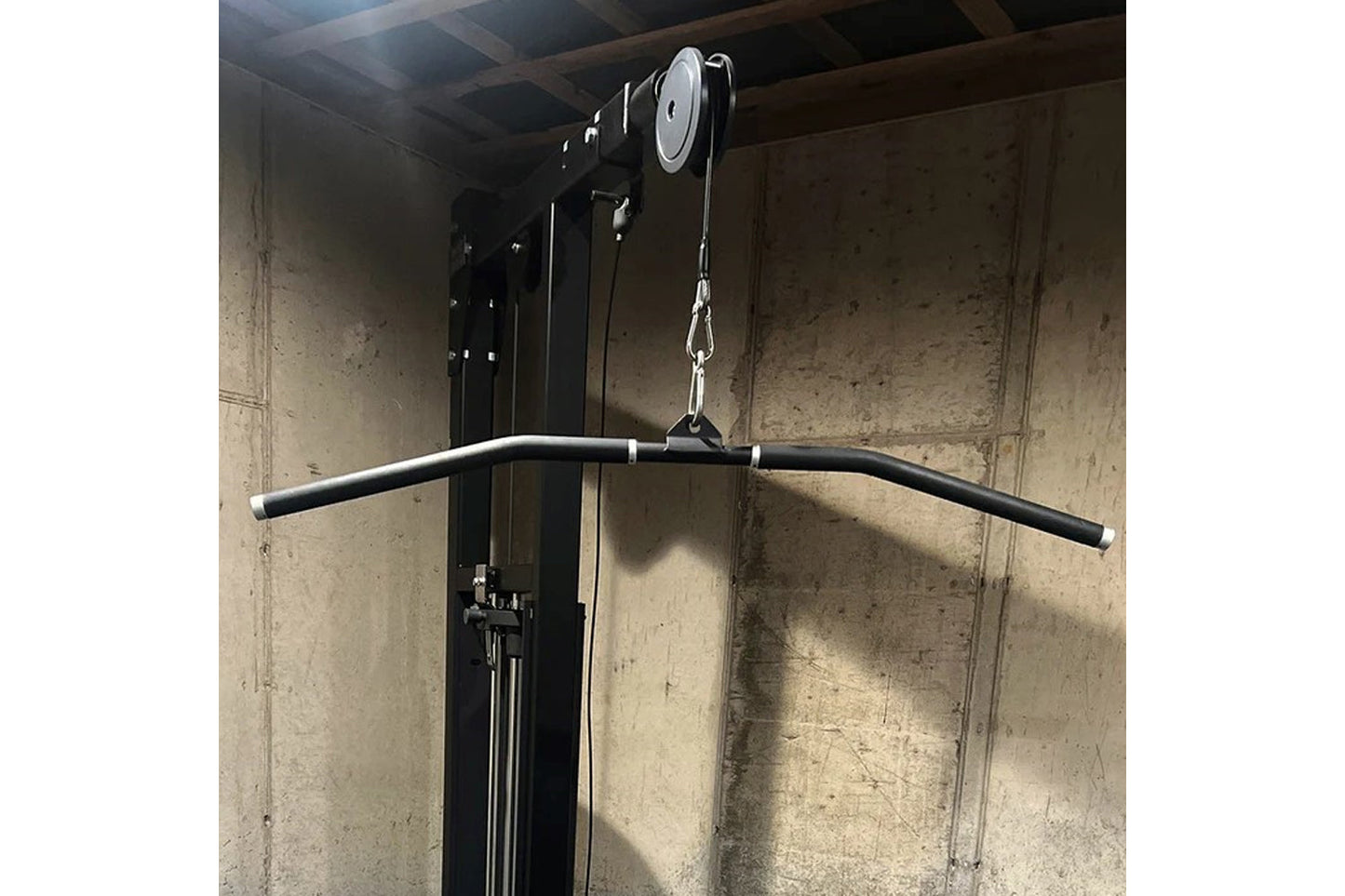 Black and silver dual pulldown/row machine with curved bar attachment and chain system, mounted on concrete wall
