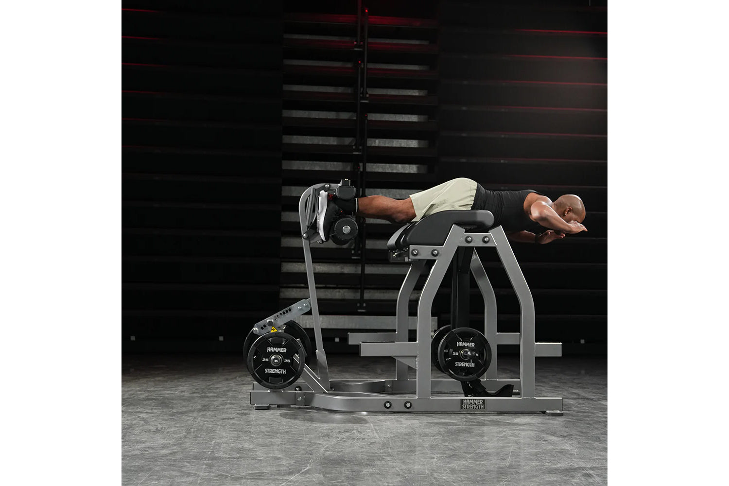 Man using gray and black Hammer Strength glute-ham reverse hyper combo bench machine with loaded weight plates in gym setting
