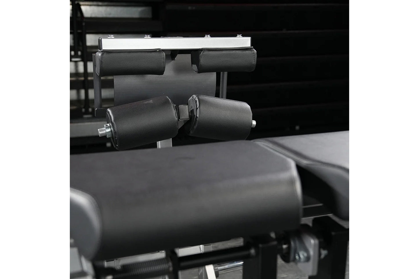 Black padded leg extension machine with cylindrical foam rollers and metal frame, gym equipment detail shot
