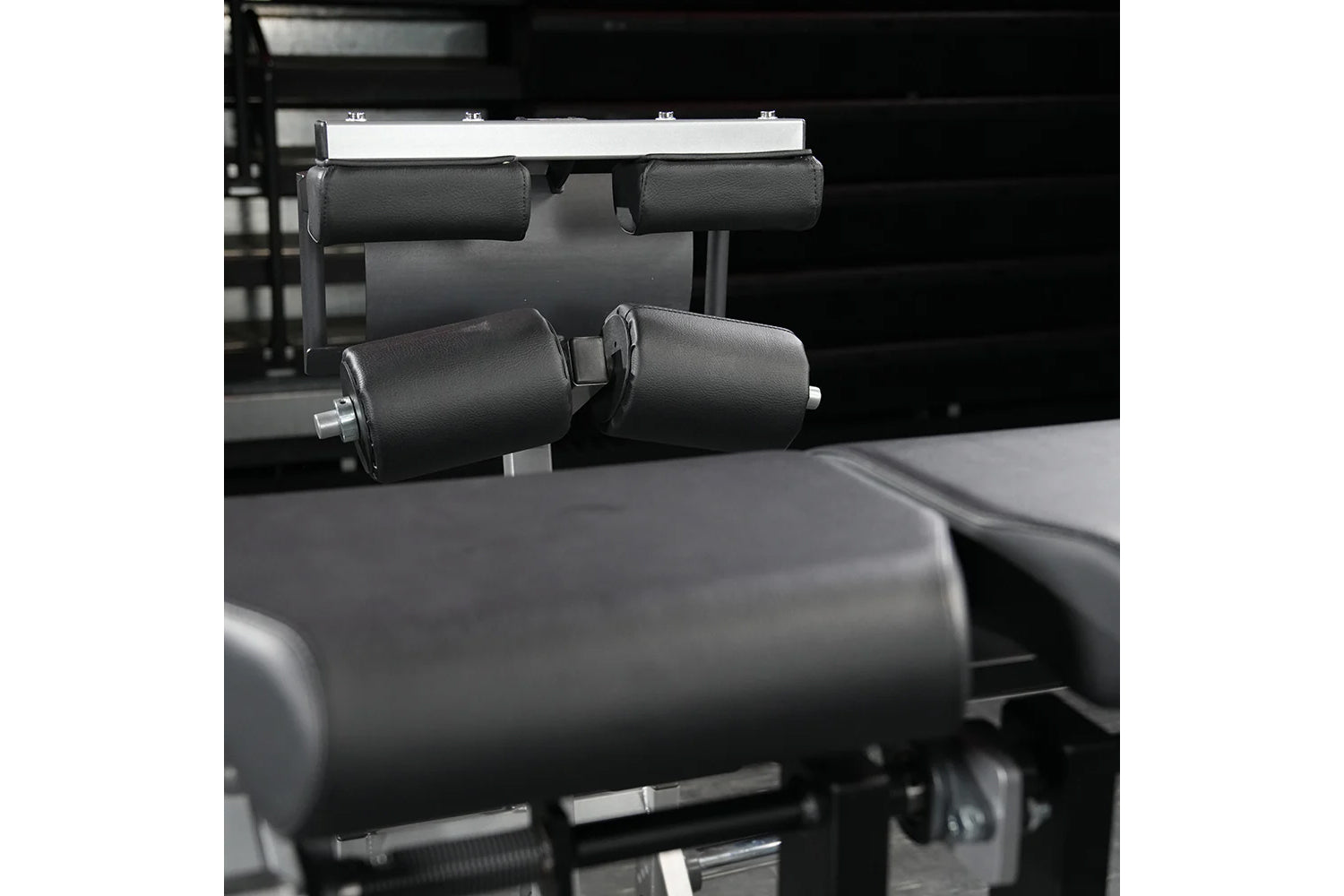 Black padded leg extension machine with cylindrical foam rollers and metal frame, gym equipment detail shot