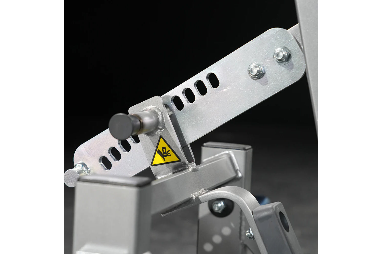 Silver metal fitness machine component with adjustment lever, ventilation slots, chrome bolts, and yellow caution warning lab