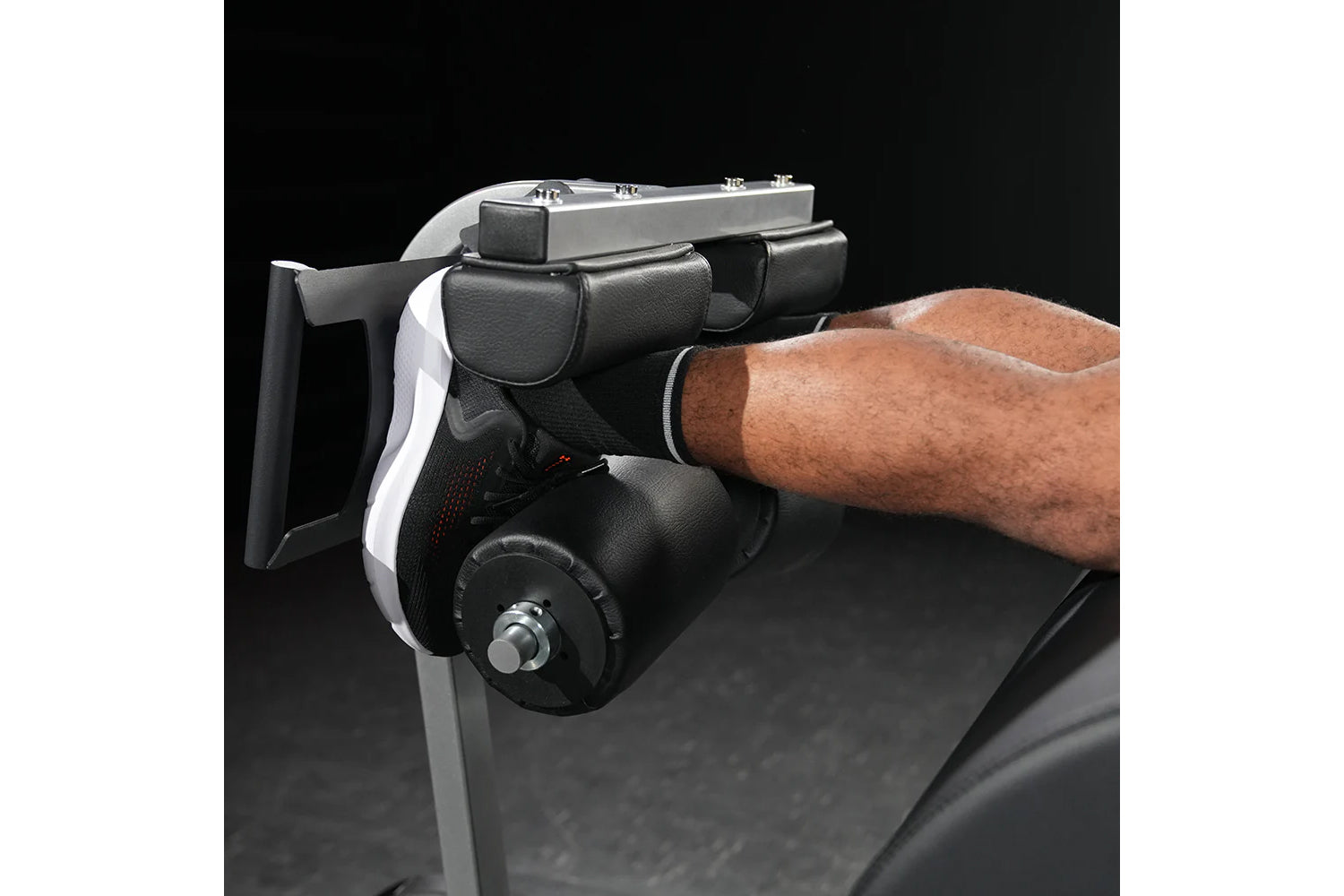Black and gray leg press machine with padded foot platform and adjustable seat, worn by model on dark background