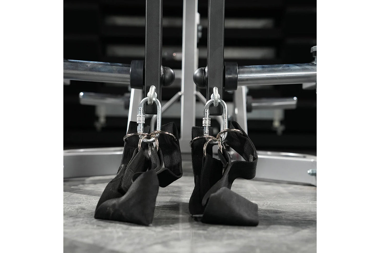 Pair of black foam handles with silver carabiners attached to gym machine equipment with metal frame and rollers