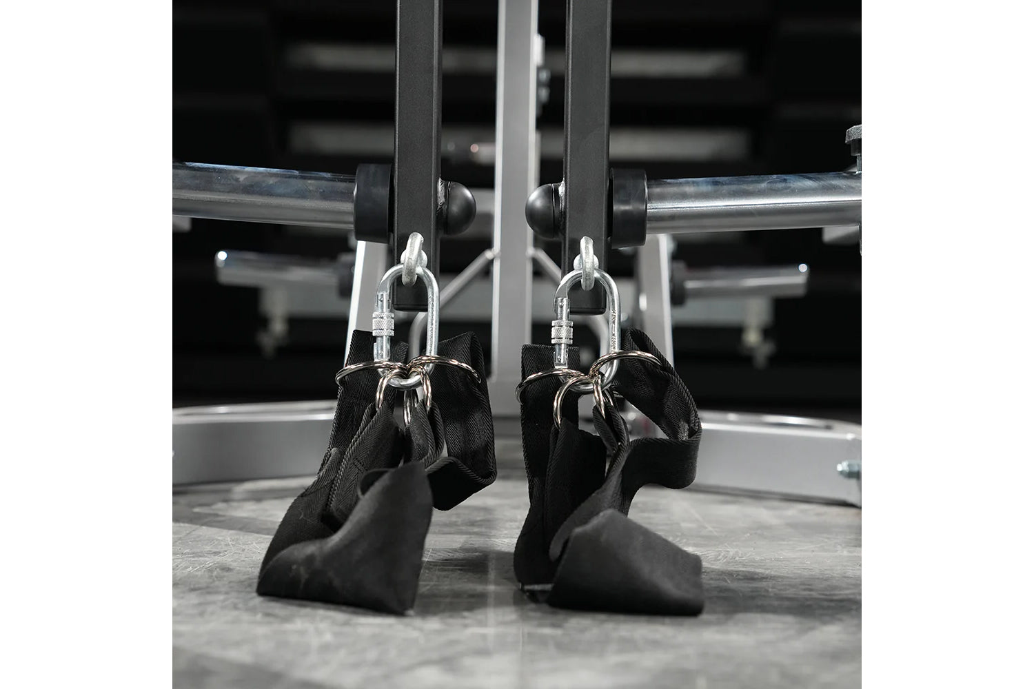 Pair of black foam handles with silver carabiners attached to gym machine equipment with metal frame and rollers