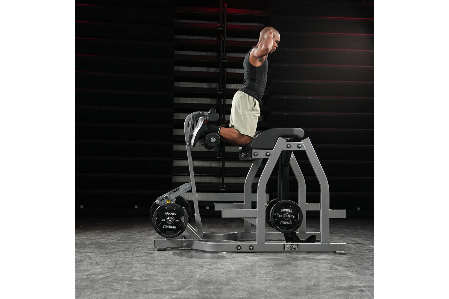 Man performing reverse hyper exercise on gray Hammer Strength machine with black weight plates in gym setting
