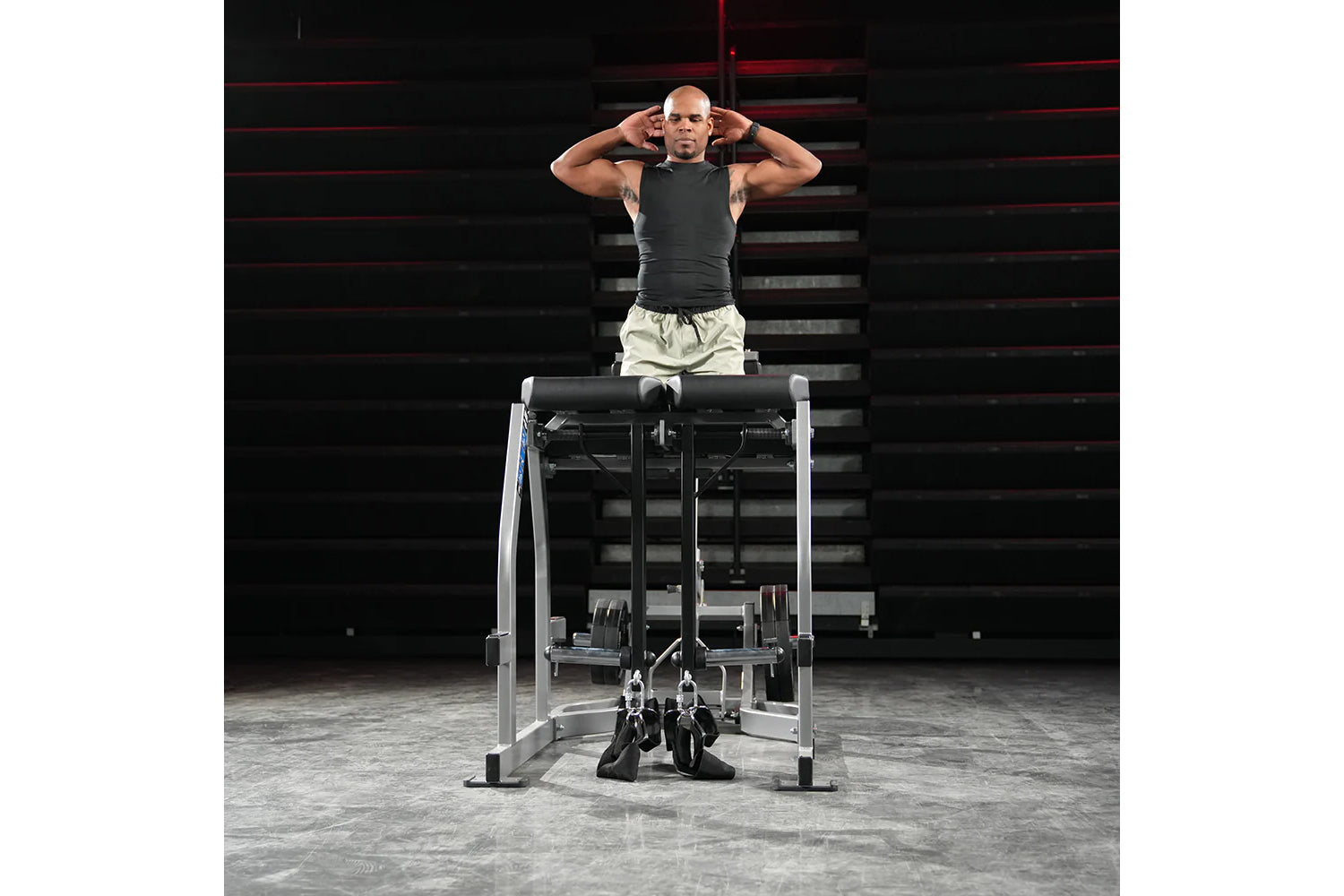 Man performing exercise on Hammer Strength Glute-Ham Reverse Hyper Combo machine, wearing charcoal tank top and cream shorts 