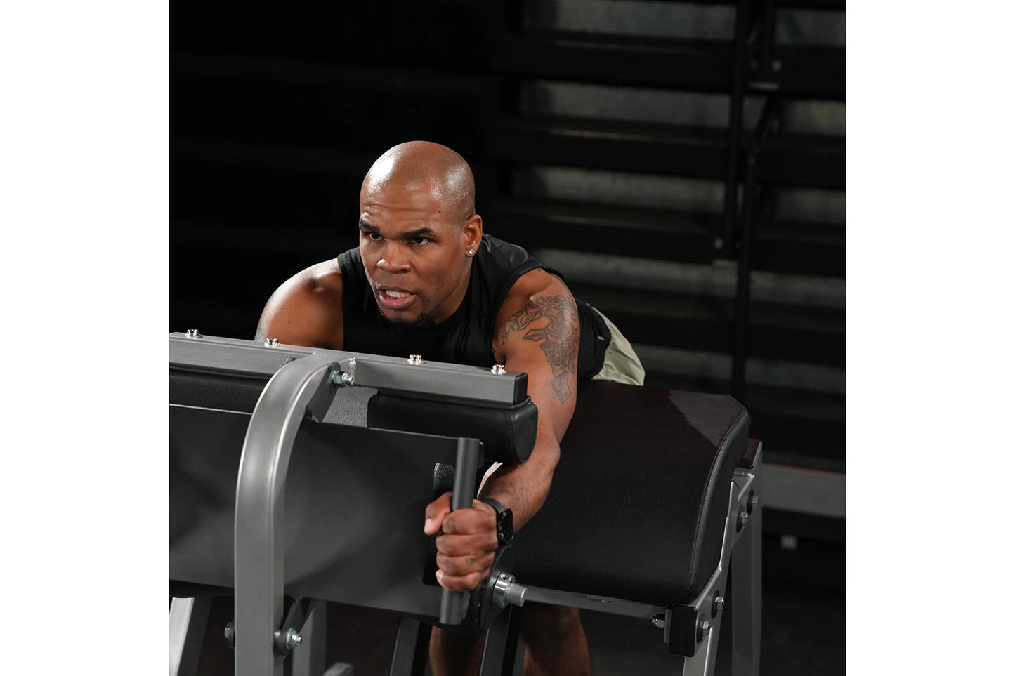 Man using black Hammer Strength Glute-Ham Reverse Hyper Combo Bench Machine in gym setting, wearing black sleeveless tank top