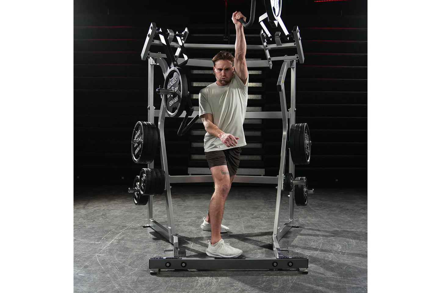Male athlete wearing light gray t-shirt and dark shorts using Hammer Strength Ground Base Jammer machine with loaded barbells