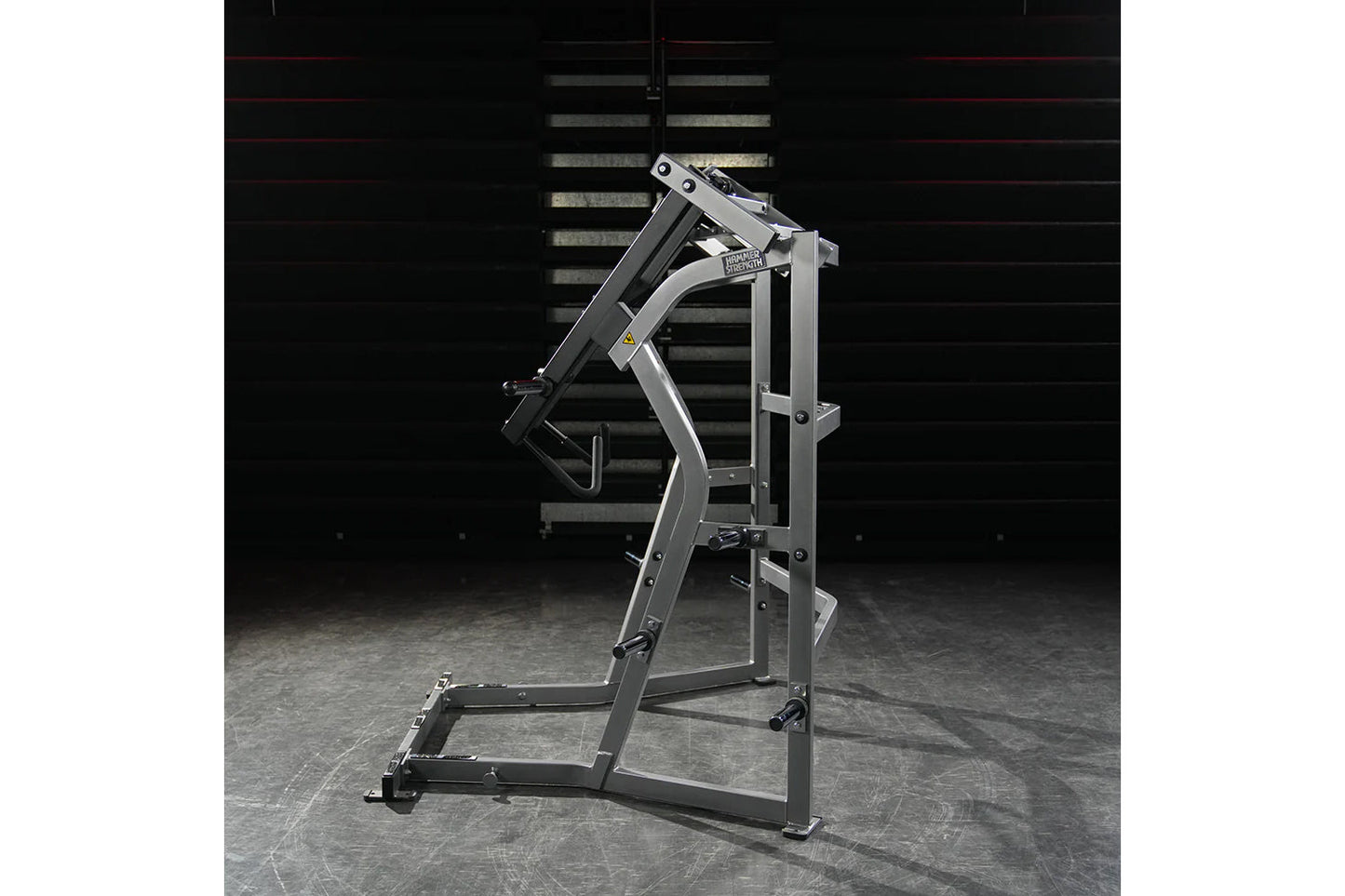 Hammer Strength Ground Base Jammer machine with silver and black frame on concrete floor against dark brick wall background