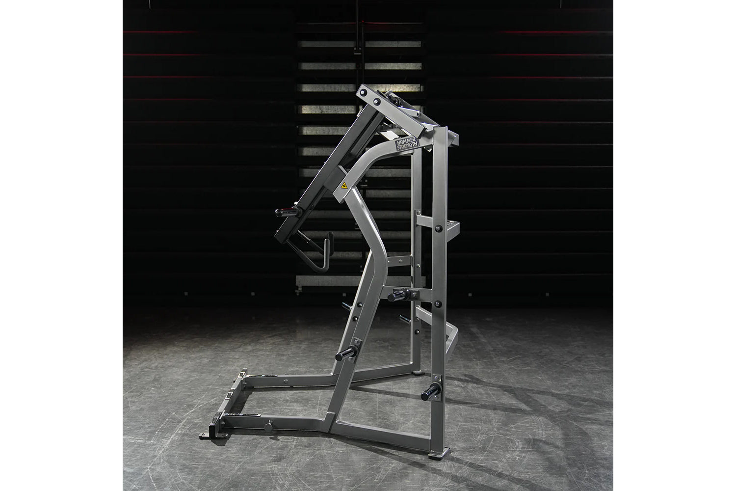 Hammer Strength Ground Base Jammer machine with silver and black frame on concrete floor against dark brick wall background