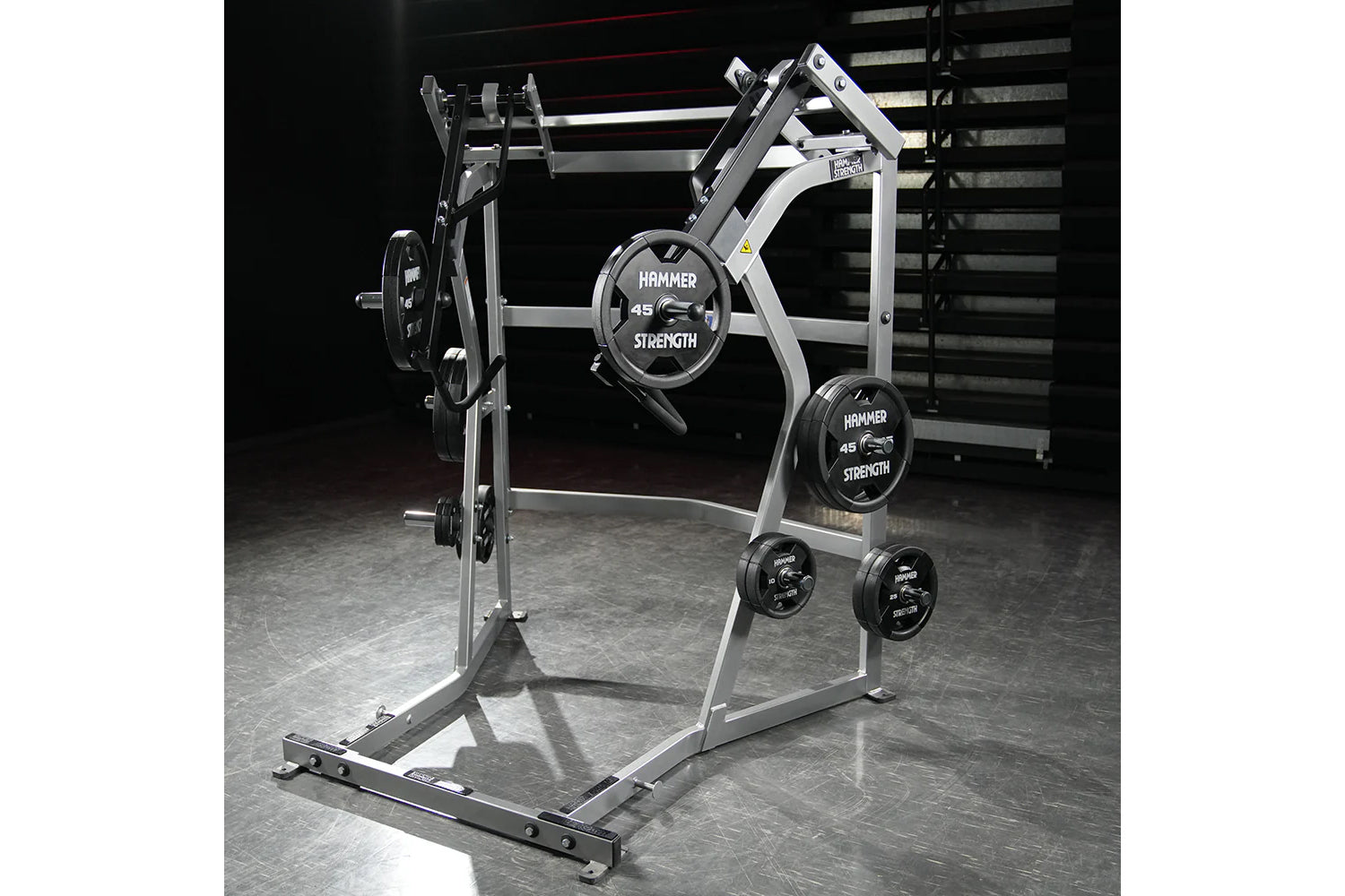 Hammer Strength Ground Base Jammer with white frame, black weight plates labeled 45 pounds, and storage pegs on gym floor
