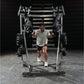 Man wearing light gray t-shirt and black shorts running through metal weight rack machine with loaded barbells in gym setting
