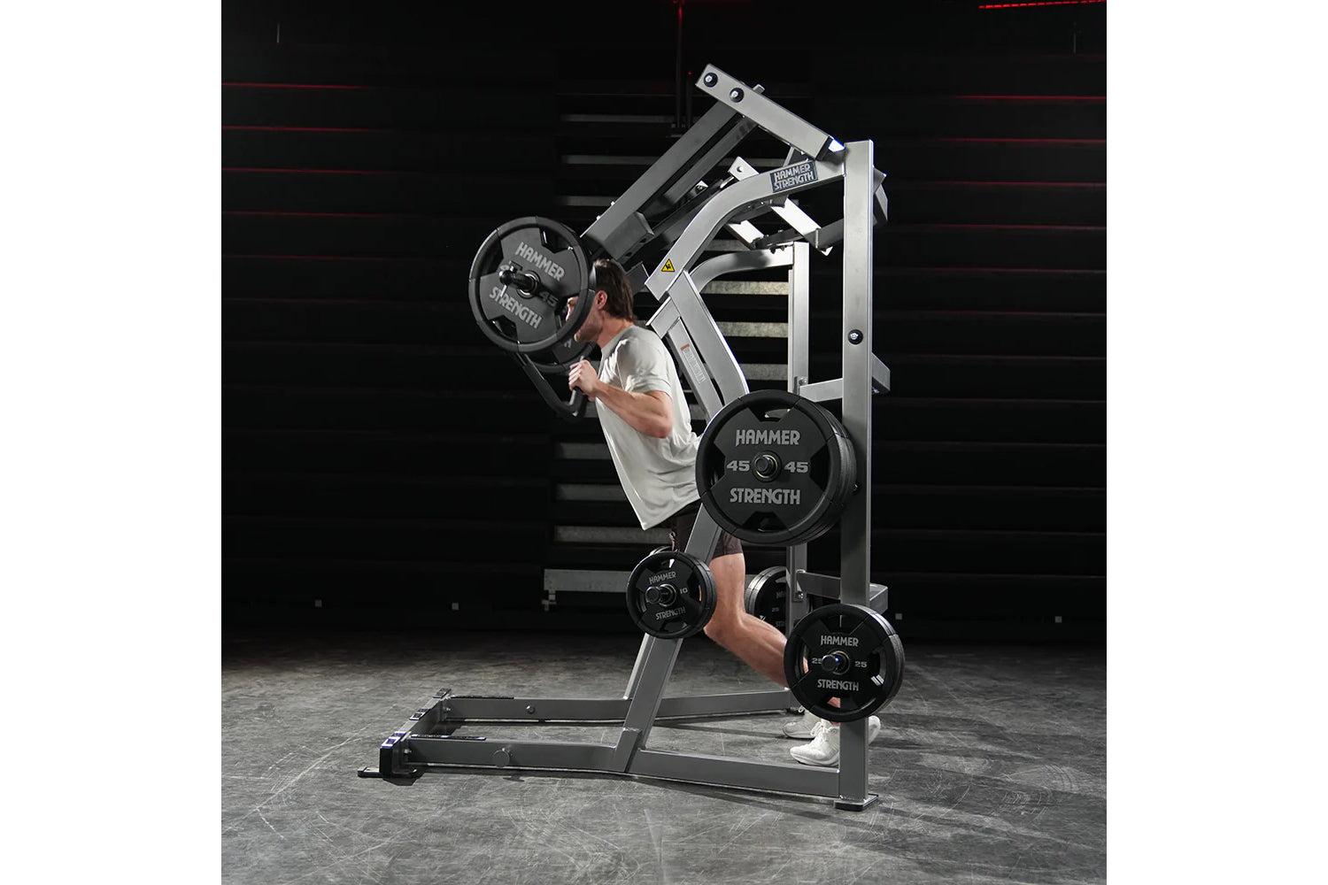 Man using Hammer Strength Ground Base Jammer machine with black weight plates in gym setting
