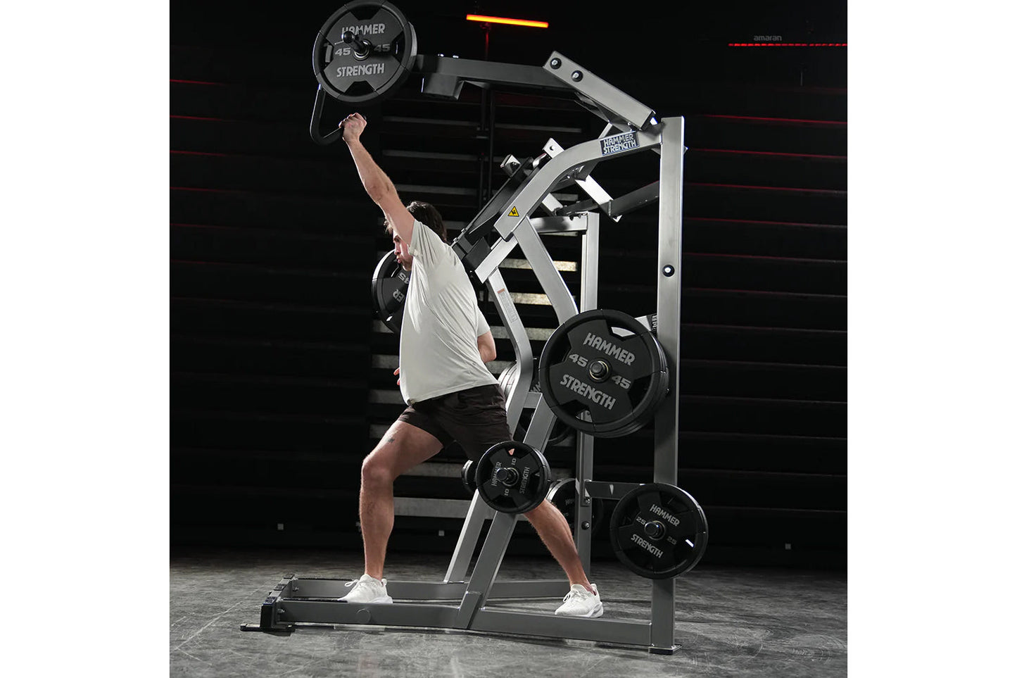 Man using Hammer Strength jammer machine with 45-lb plate, white and black metal frame, gym setting with red rope background