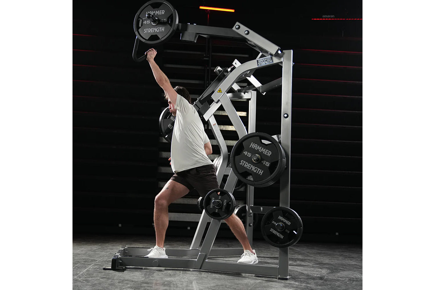 Man using Hammer Strength jammer machine with 45-lb plate, white and black metal frame, gym setting with red rope background