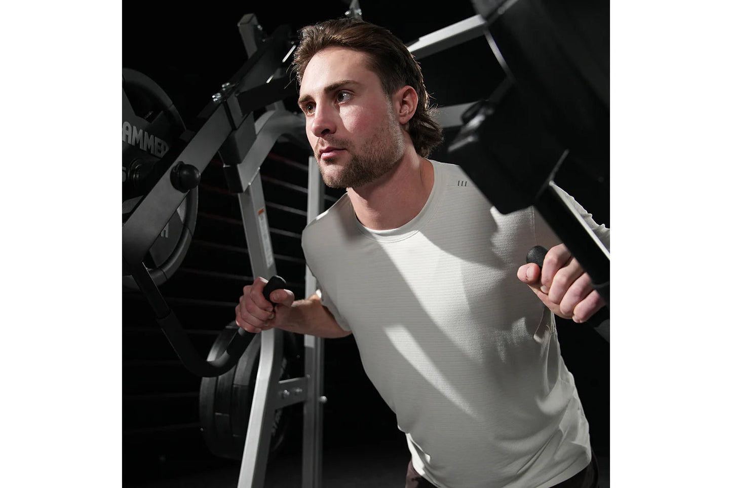 Man wearing light gray t-shirt using Hammer Strength black and gray jammer machine with handles during workout