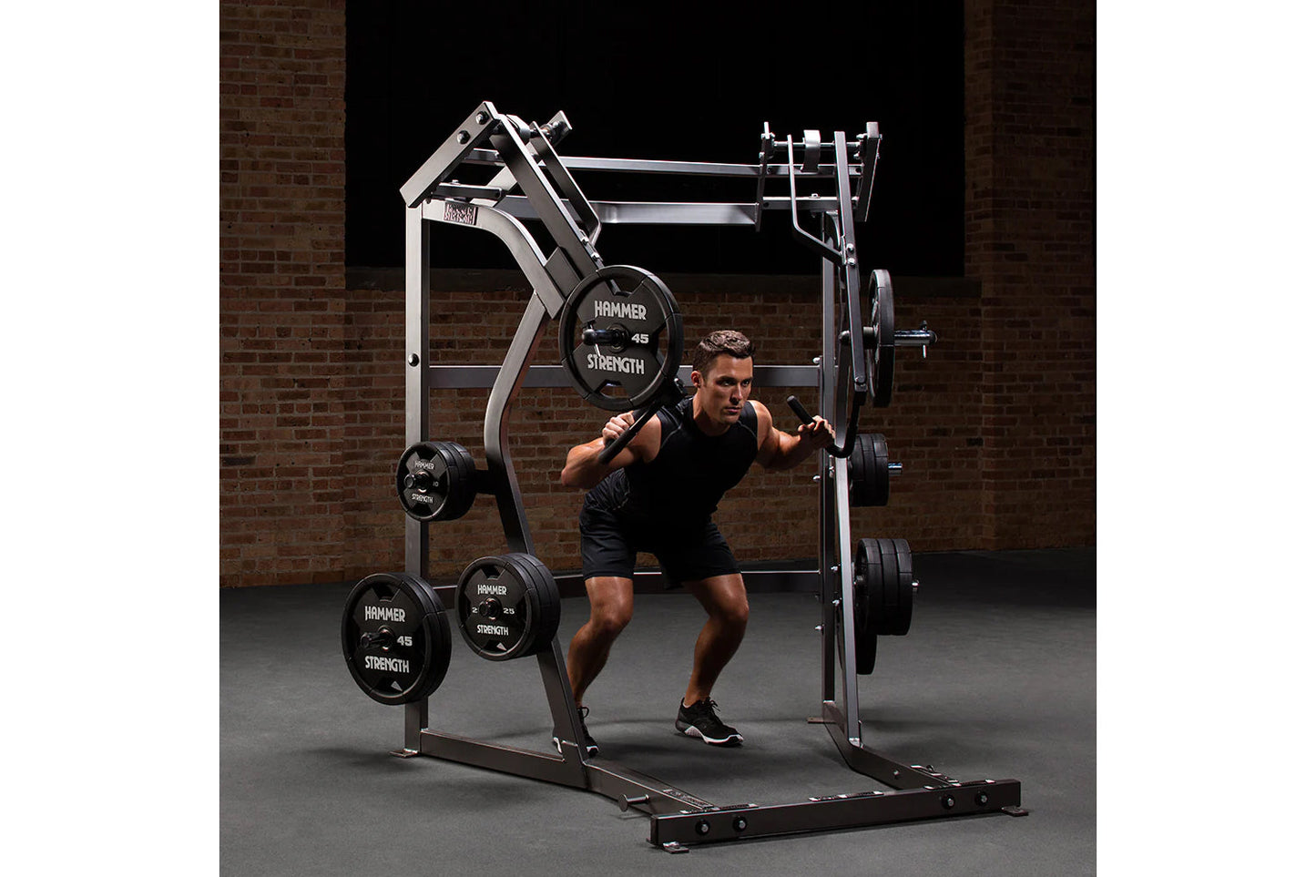 Male athlete using Hammer Strength black and silver ground base jammer machine with loaded weight plates in gym setting