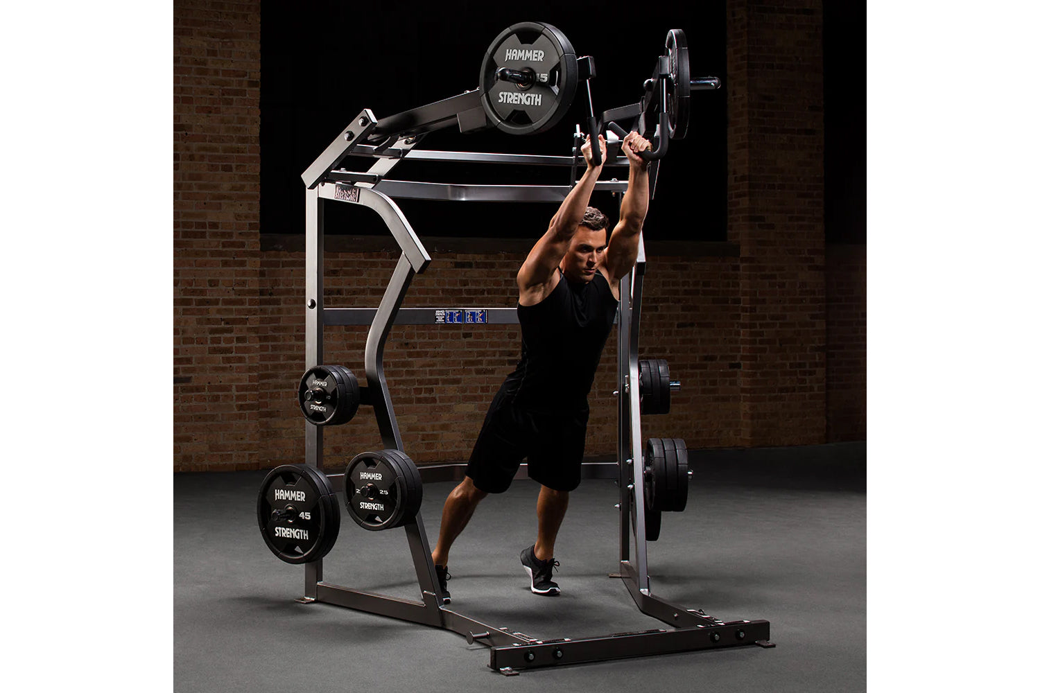 Man performing shoulder press on Hammer Strength black and silver jammer machine with weight plates