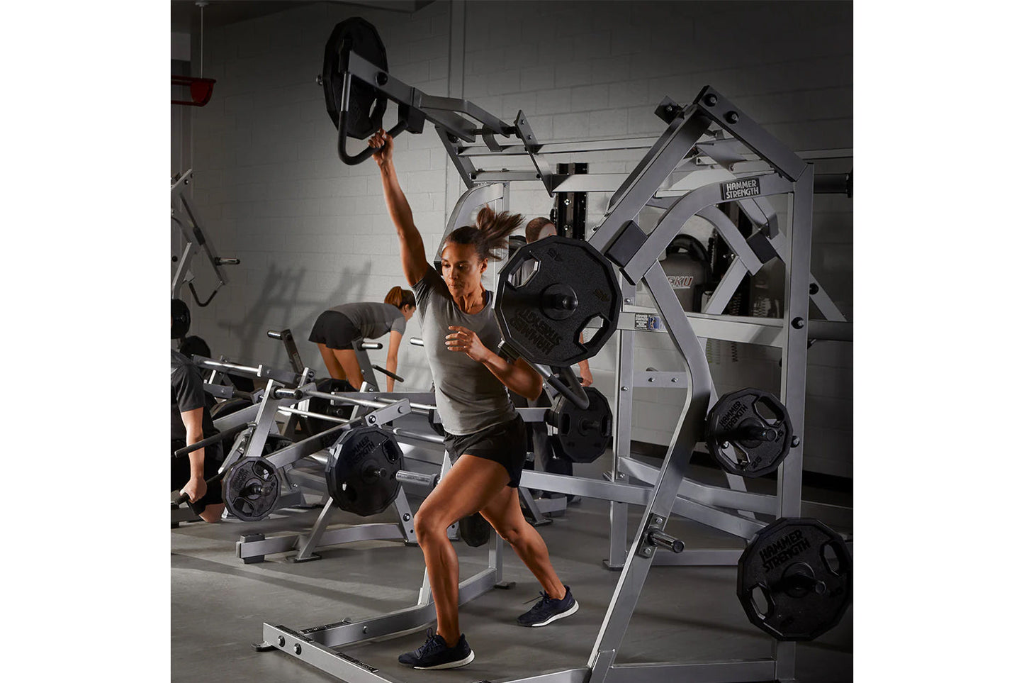 Woman using Hammer Strength jammer machine with loaded weight plates in a gym setting