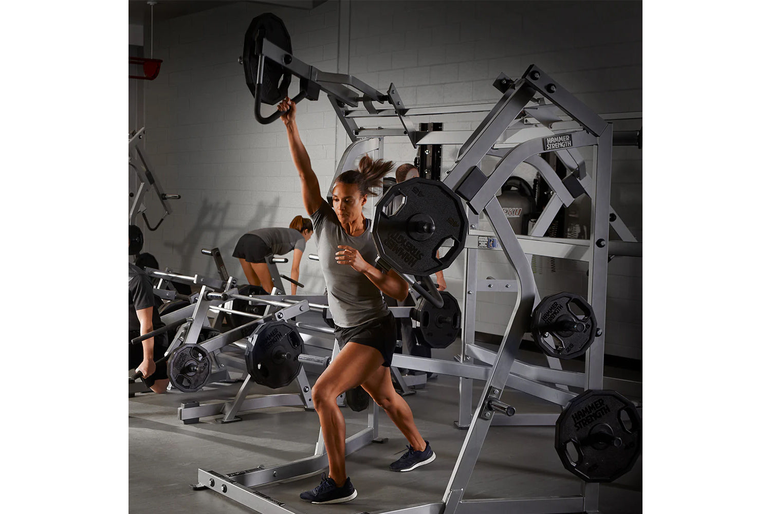 Woman using Hammer Strength jammer machine with loaded weight plates in a gym setting