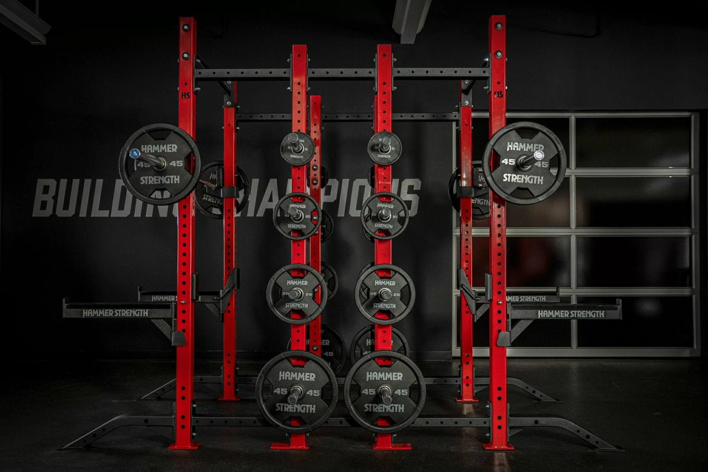 Hammer Strength red and black half combo power rack with loaded Olympic weight plates and barbell sleeves in gym setting
