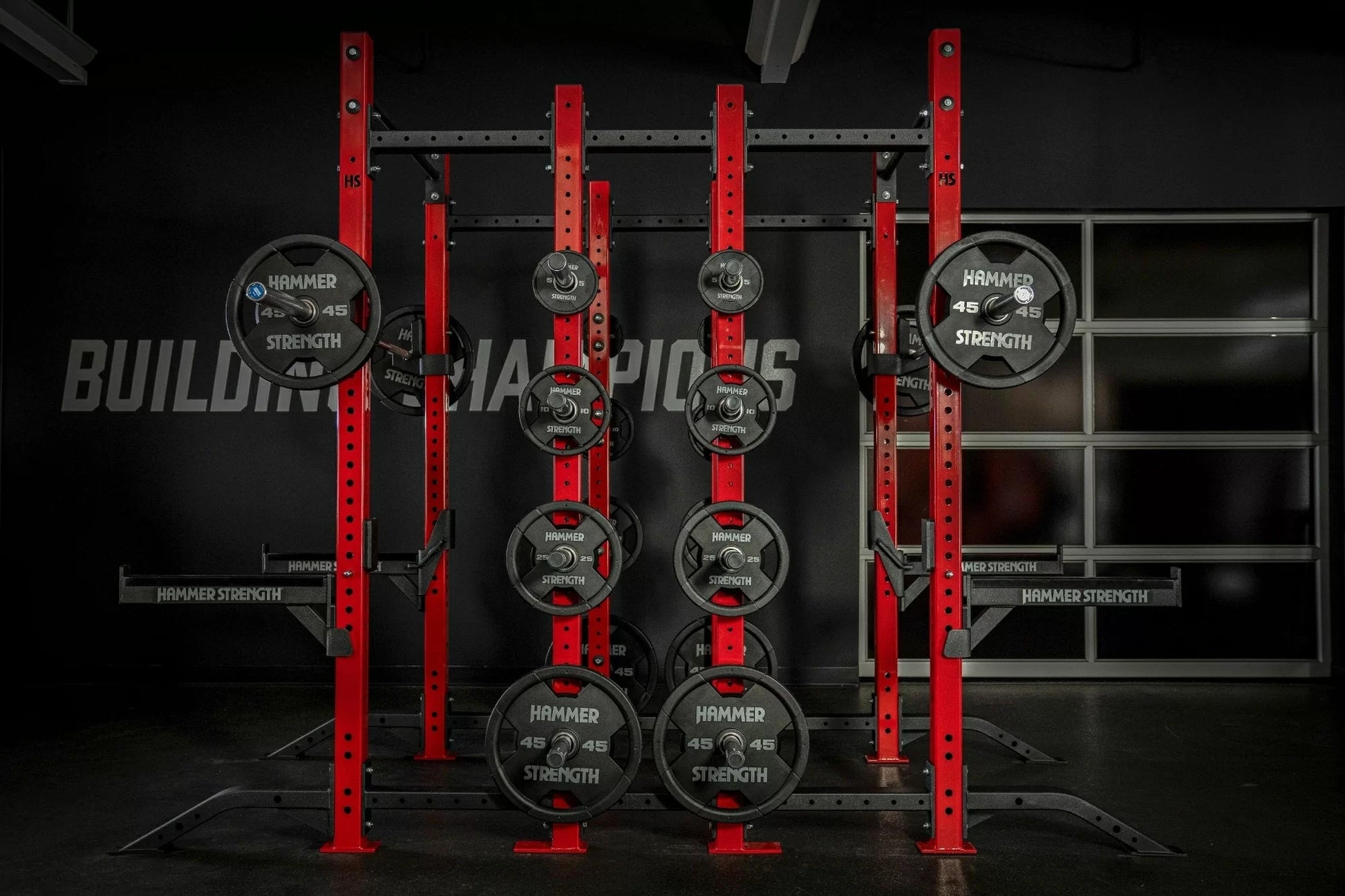 Hammer Strength red and black half combo power rack with loaded Olympic weight plates and barbell sleeves in gym setting