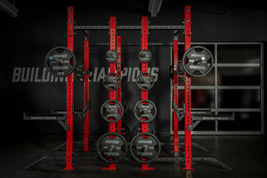 Hammer Strength red and black half combo power rack with loaded Olympic weight plates and barbell sleeves in gym setting