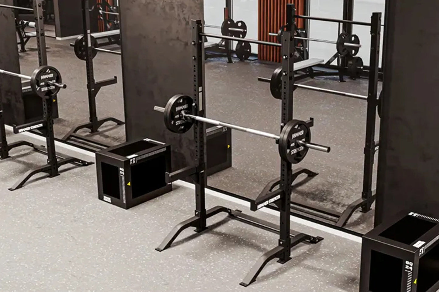 Black power squat stand with adjustable barbell safety arms and weight plate storage, shown in gym setting with loaded barbel
