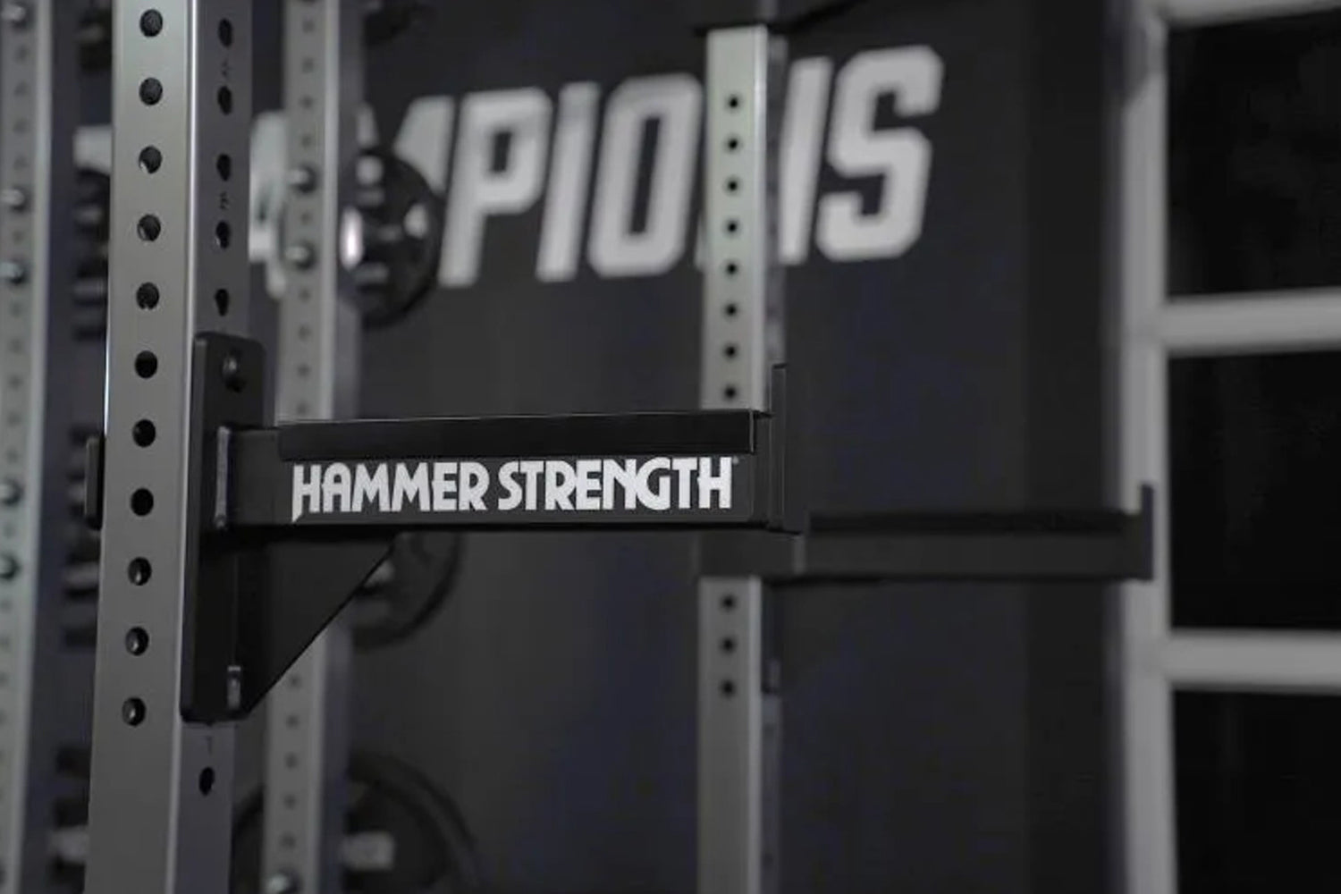 Black Hammer Strength barbell pad attached to perforated steel weight rack uprights in gym setting