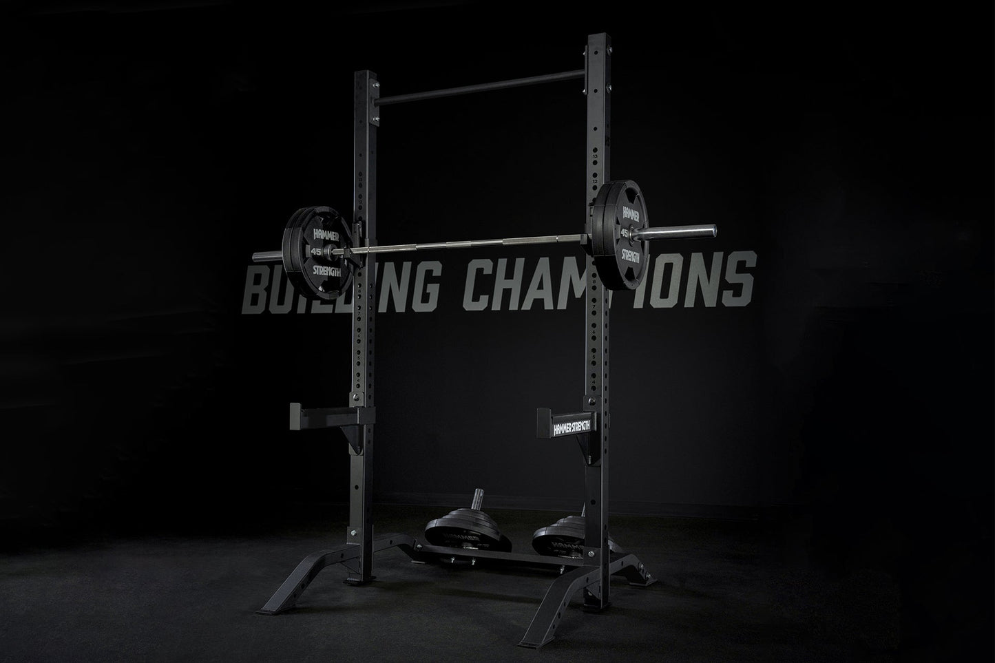 Black Hammer Strength squat stand with loaded barbell, weight plates, and safety bars on dark background