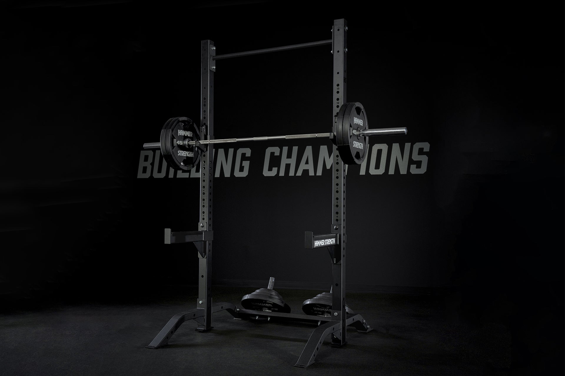 Black Hammer Strength squat stand with loaded barbell, weight plates, and safety bars on dark background