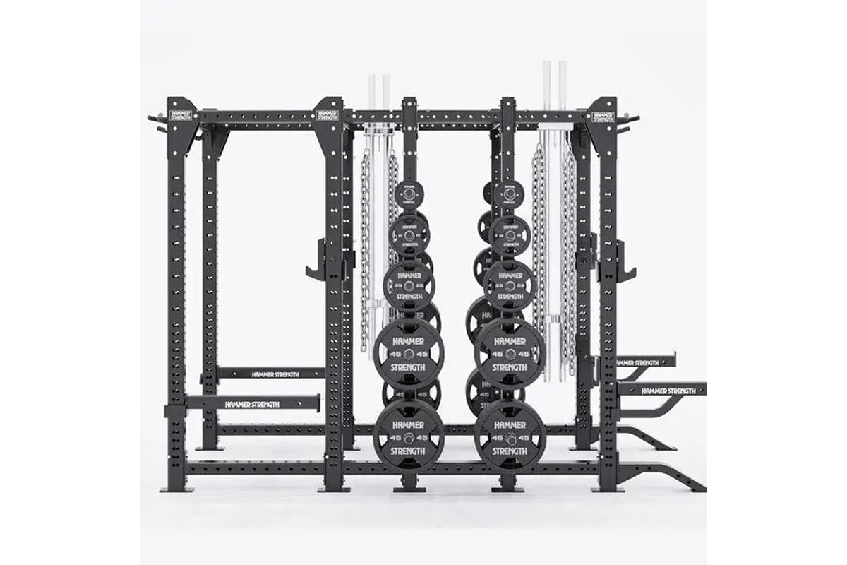 Black steel multi-station gym rack with weight plates and cable systems on white background