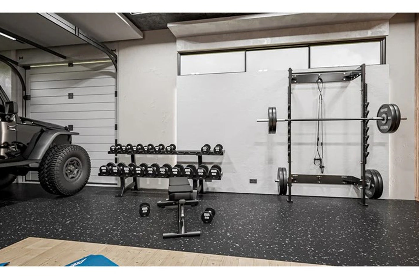 Black steel squat rack with weight plates and barbell in modern garage gym setting with rubber flooring