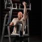 Man using gray and black Hammer Strength iso-lateral high row machine, wearing beige t-shirt with "HAMMER" logo, demonstratin