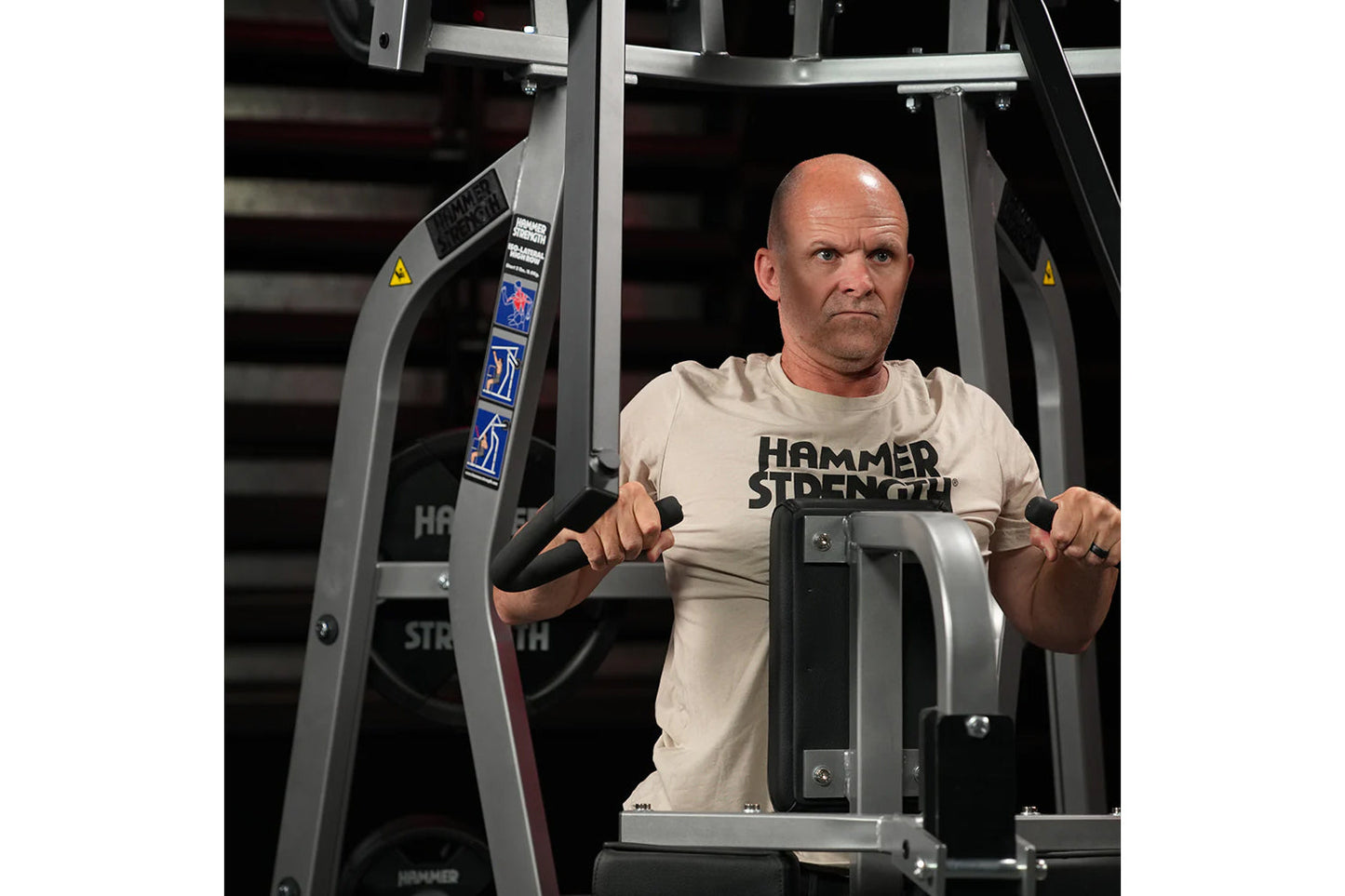 Man wearing beige Hammer Strength t-shirt using gray and black Hammer Strength Iso-Lateral High Row machine in gym setting