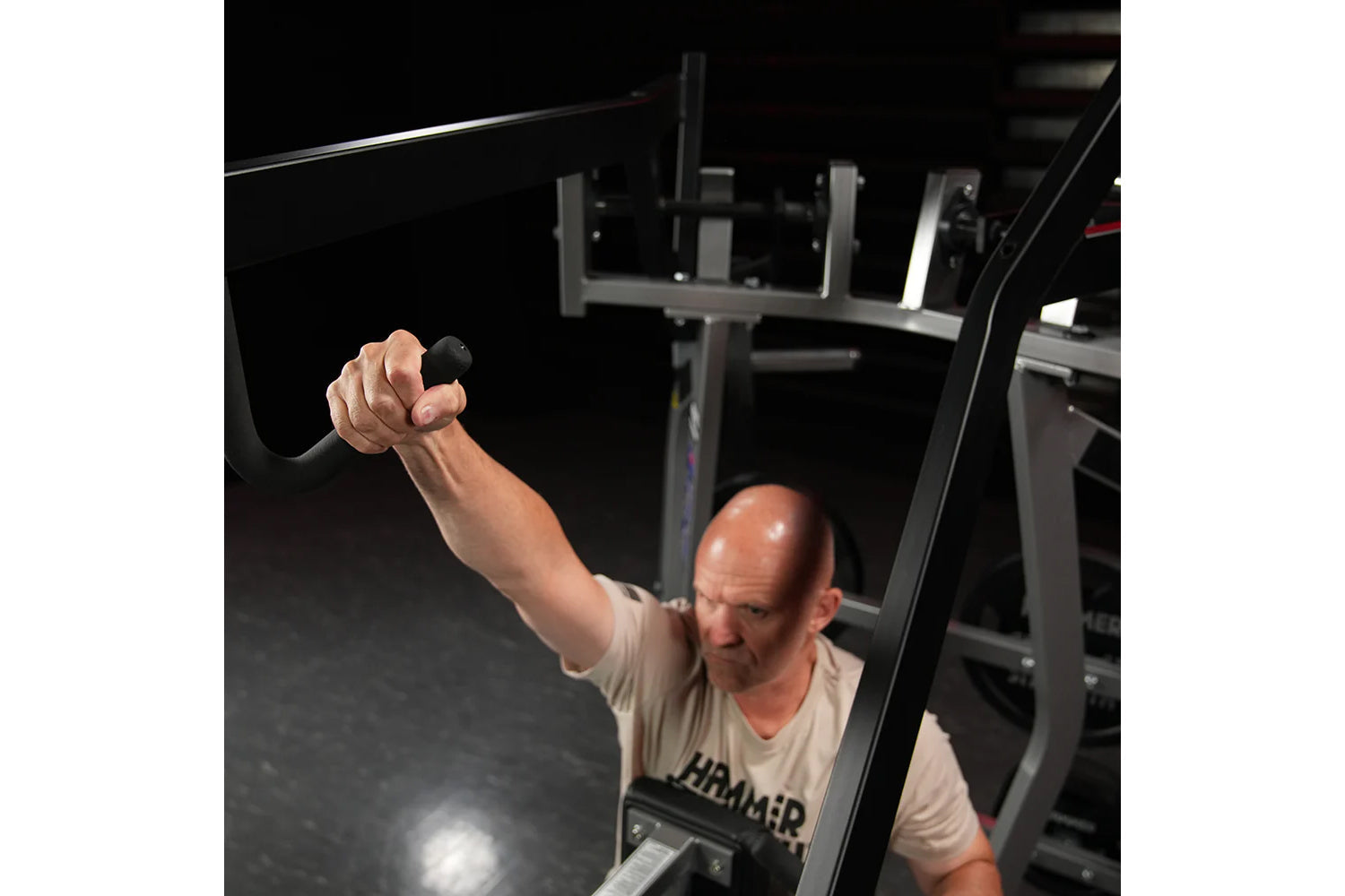 Man using black Hammer Strength iso-lateral high row machine with extended arm, demonstrating exercise form in gym setting