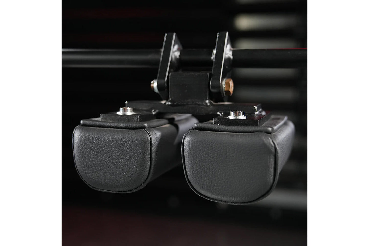 Pair of black leather neck exercise machine attachments with silver hardware and adjustable headrest pads, flat lay on dark b