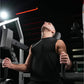 Man using black Hammer Strength plate-loaded neck exercise machine in gym setting with red neon lighting