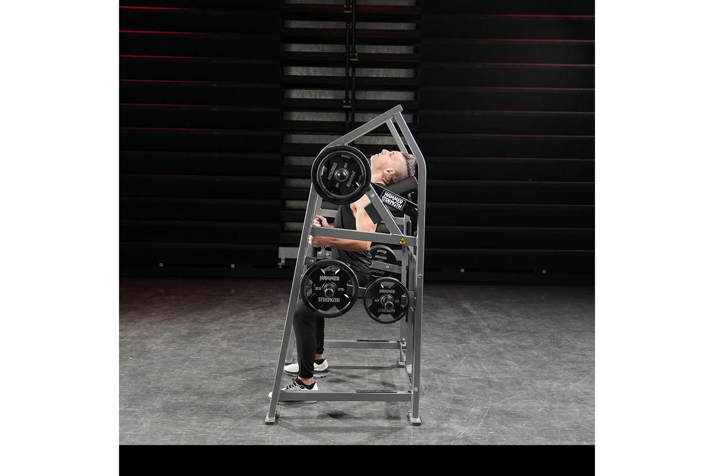 Man using gray Hammer Strength plate-loaded neck exercise machine with black weight plates in gym setting