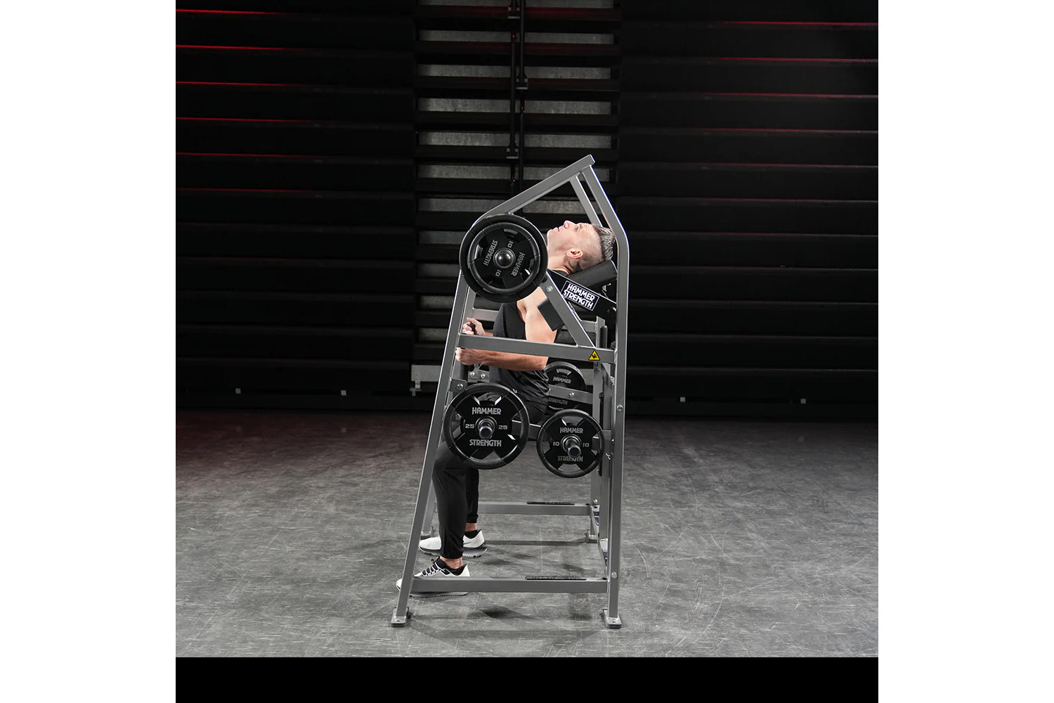 Man using gray Hammer Strength plate-loaded neck exercise machine with black weight plates in gym setting