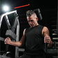 Man wearing black sleeveless tank top using gray Hammer Strength plate-loaded neck exercise machine in gym setting