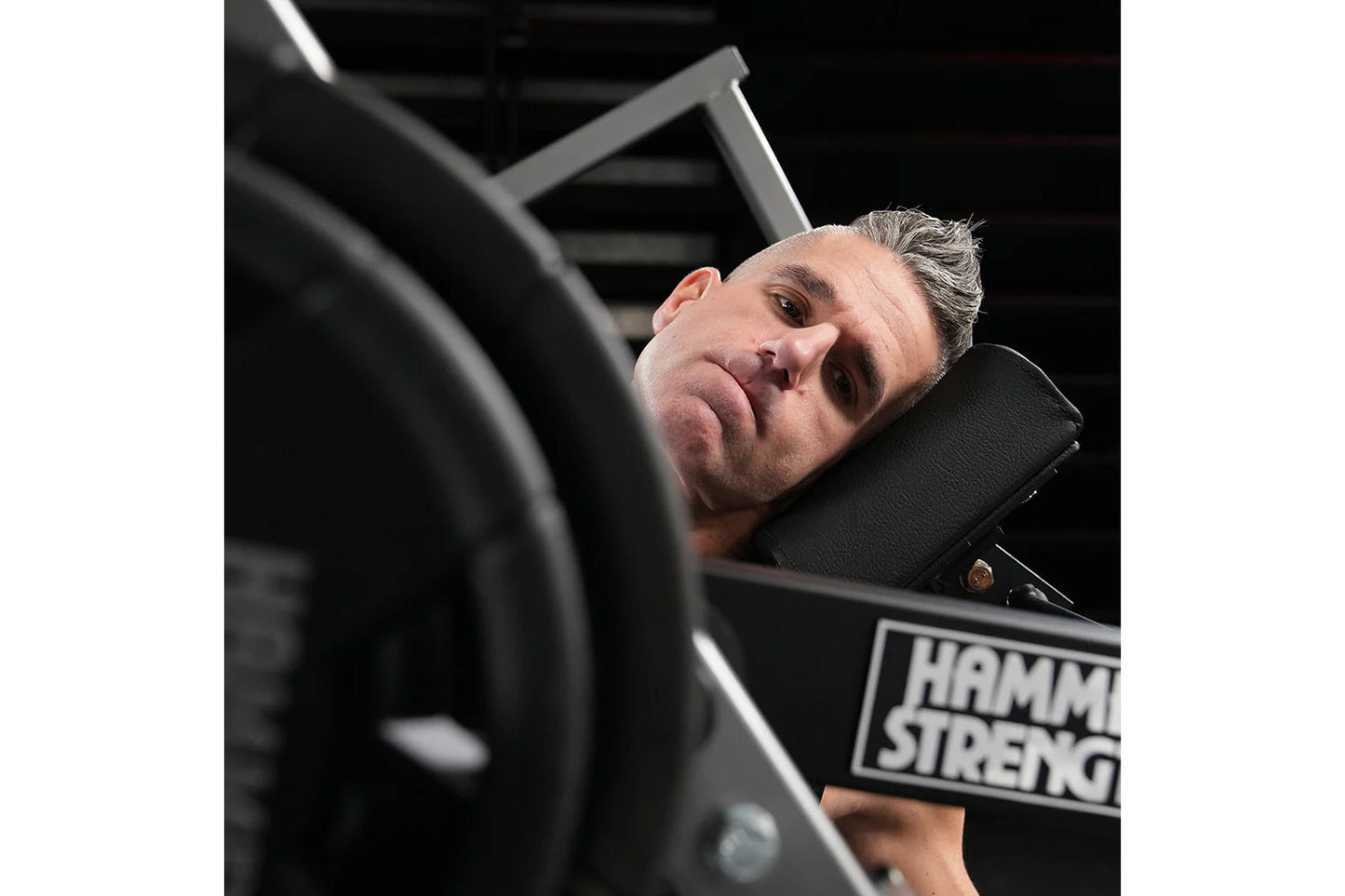 Man using black Hammer Strength plate-loaded neck exercise machine, tilting head back on padded support