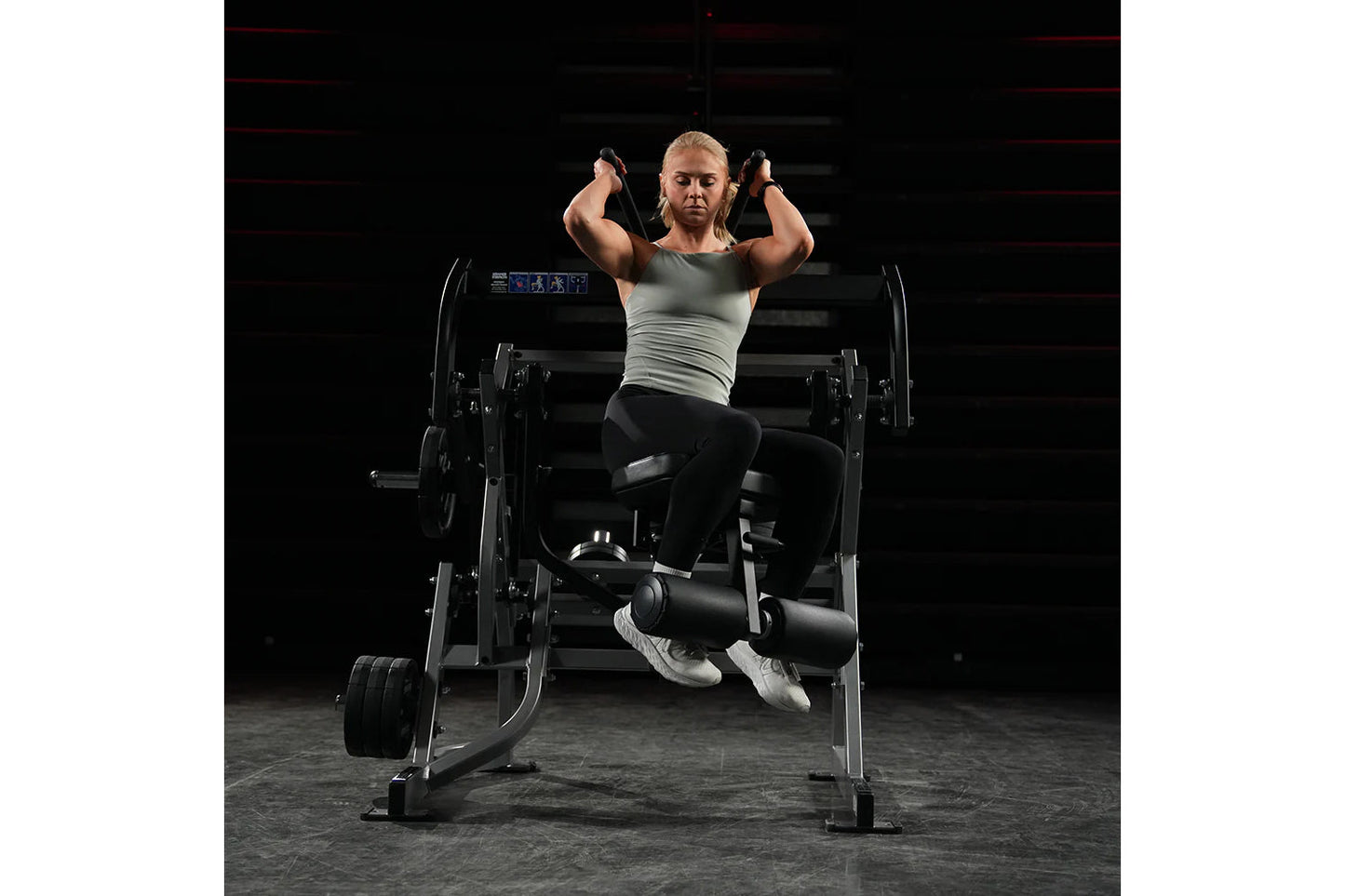 Woman performing abdominal oblique crunch exercise on black Hammer Strength plate-loaded machine in gym setting