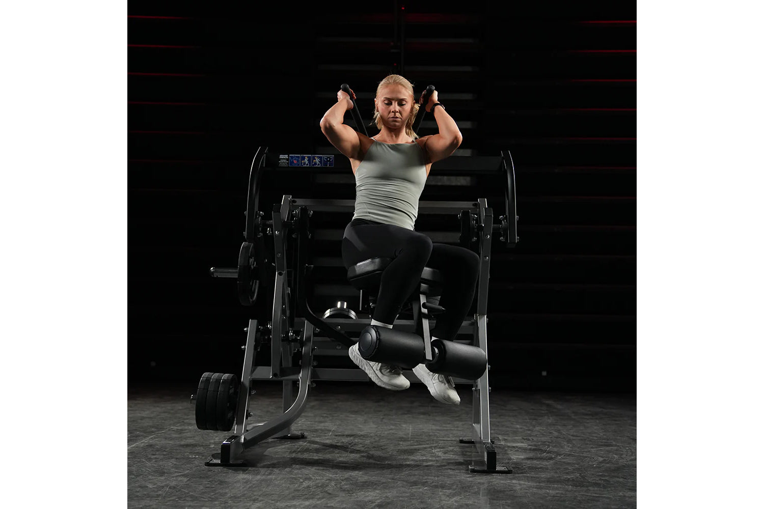 Woman performing abdominal oblique crunch exercise on black Hammer Strength plate-loaded machine in gym setting