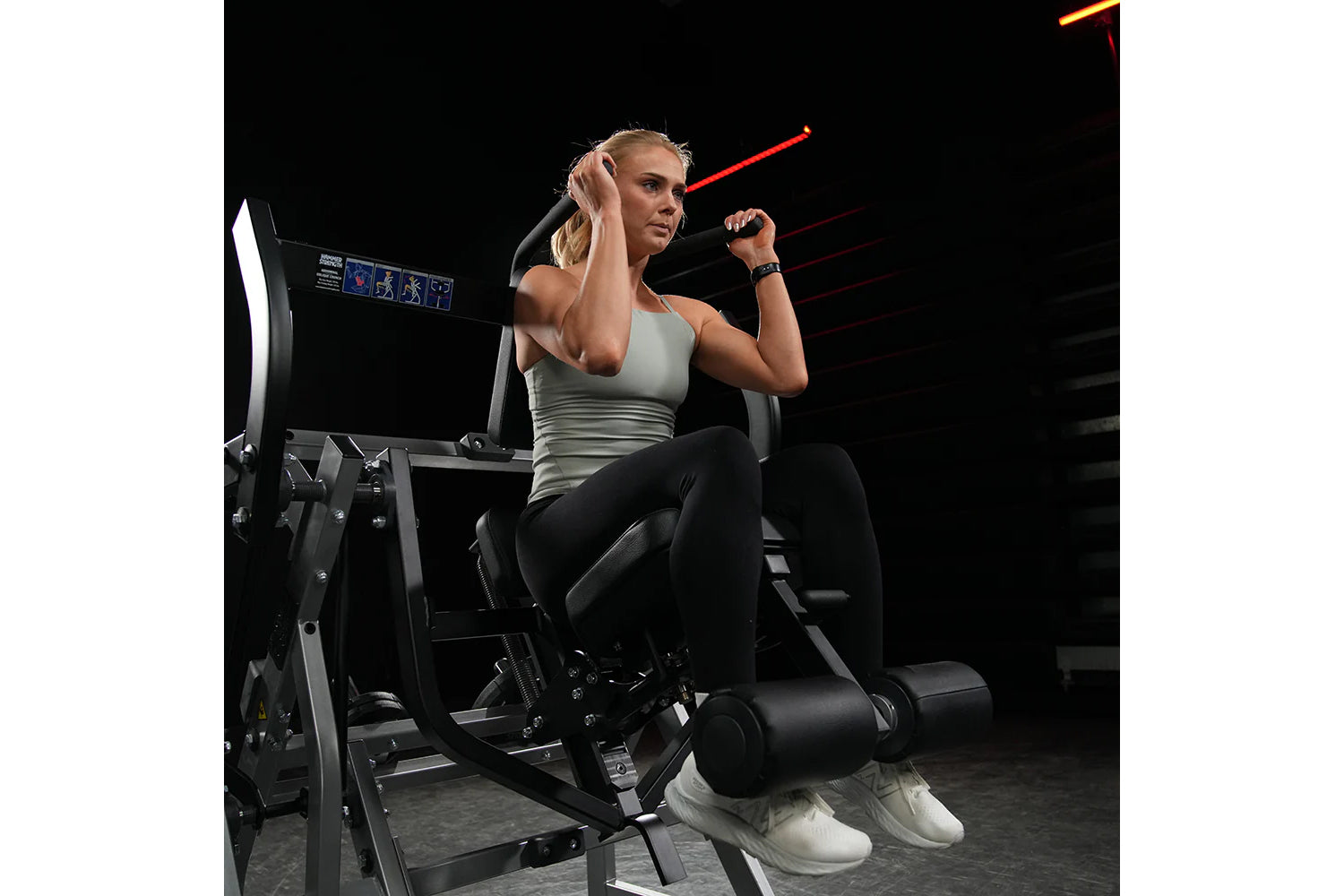 Woman wearing gray sleeveless tank top and black leggings using Hammer Strength plate-loaded abdominal oblique crunch machine