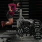 Woman in burgundy t-shirt and black shorts using Hammer Strength plate-loaded belt squat machine with weight plates, stairs i